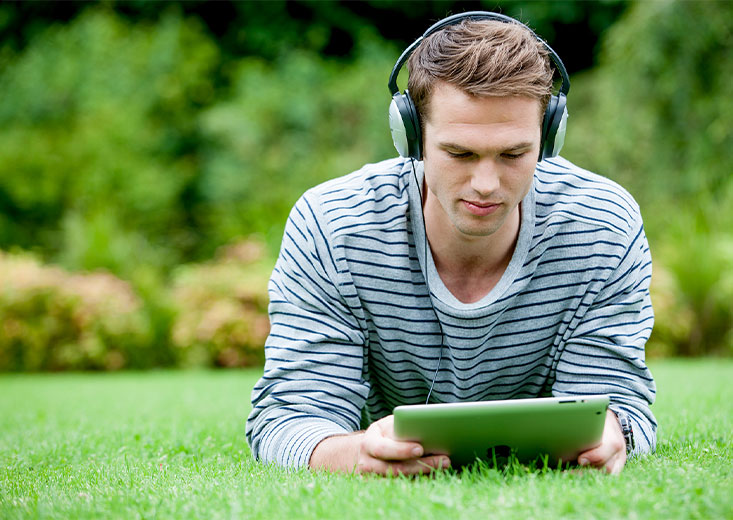 Online La Trobe student studying on a tablet laying in the grass.